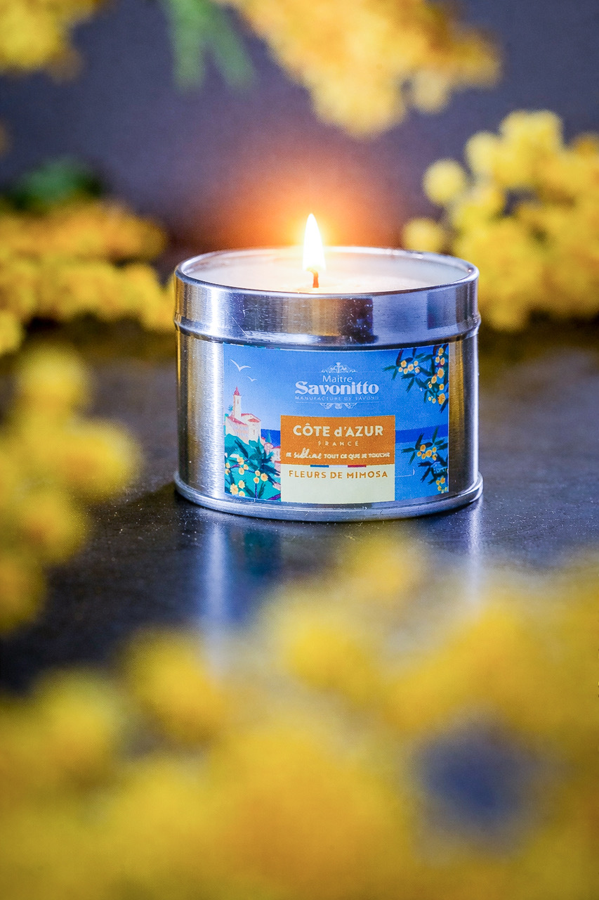 Bougie parfumée au mimosa dans une boîte métal, entourée de fleurs jaunes, ambiance chaleureuse