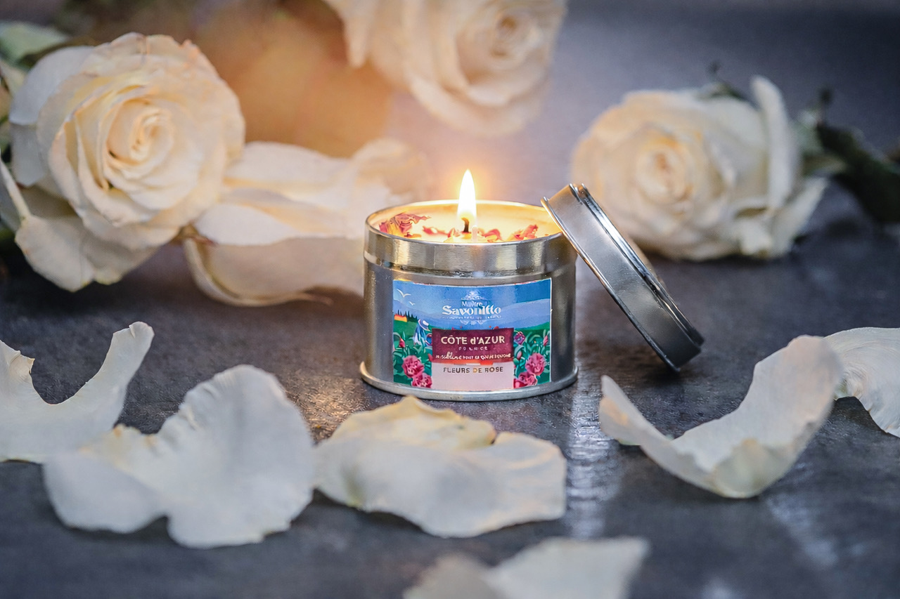 Bougie parfumée à la rose dans une boîte métal, entourée de pétales de rose blanche, ambiance élégante